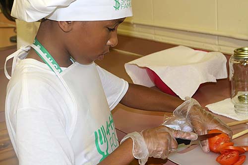 Participant in the 4-H Healthy Habits cooking camp cuts a tomato.