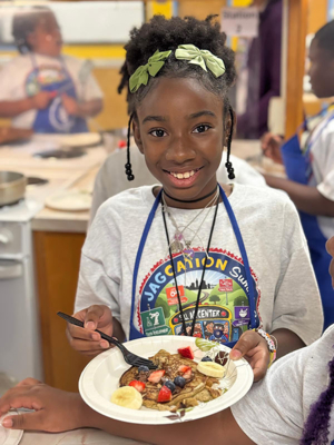 A 2025 JAGcation Summer Camp participant shows the whole-wheat pancakes topped with fresh fruit that she cooked during the camp.