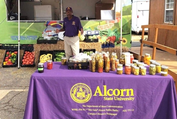 Alcorn State University Facility Manager Percy Baldwin stands in front of the Cotton Ball Express Mobile Farmers Market while surrounded by fruits and vegetables.