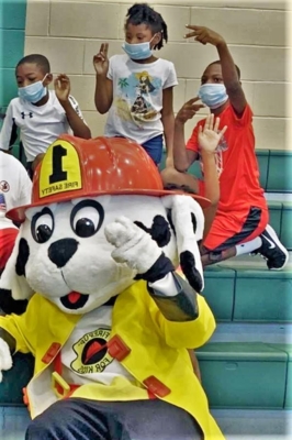 Vicksburg Fire Department mascot sits with three students on the bleachers.