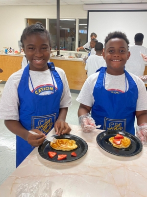 Two students display the pancakes they learned to cook during a session in the JAGcation summer camp.