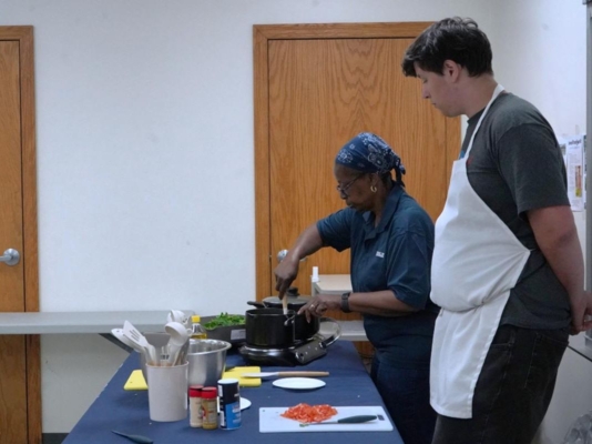 Two people cooking at a table set up like a kitchen.